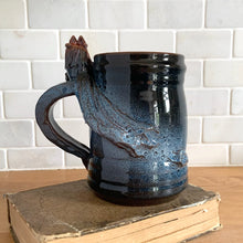 Load image into Gallery viewer, Rare vintage handmade Poseidon and Mermaid redware pottery mug finished in high fired two tone blue glaze on the exterior and a clear glazed interior. This large mug features a figural god of the sea wrapped around the exterior and mermaid in the interior of the mug. Crafted by KD Gandas, Lithuania 1990s. The perfect vessel for your favourite hot beverage!

In excellent condition with original sticker and impressed maker&#39;s mark.

Measures 6 1/4 x 4 1/4 x 6 1/2 inches (incl. handle)

Capacity 16 ounces
