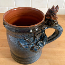 Load image into Gallery viewer, Rare vintage handmade Poseidon and Mermaid redware pottery mug finished in high fired two tone blue glaze on the exterior and a clear glazed interior. This large mug features a figural god of the sea wrapped around the exterior and mermaid in the interior of the mug. Crafted by KD Gandas, Lithuania 1990s. The perfect vessel for your favourite hot beverage!

In excellent condition with original sticker and impressed maker&#39;s mark.

Measures 6 1/4 x 4 1/4 x 6 1/2 inches (incl. handle)

Capacity 16 ounces
