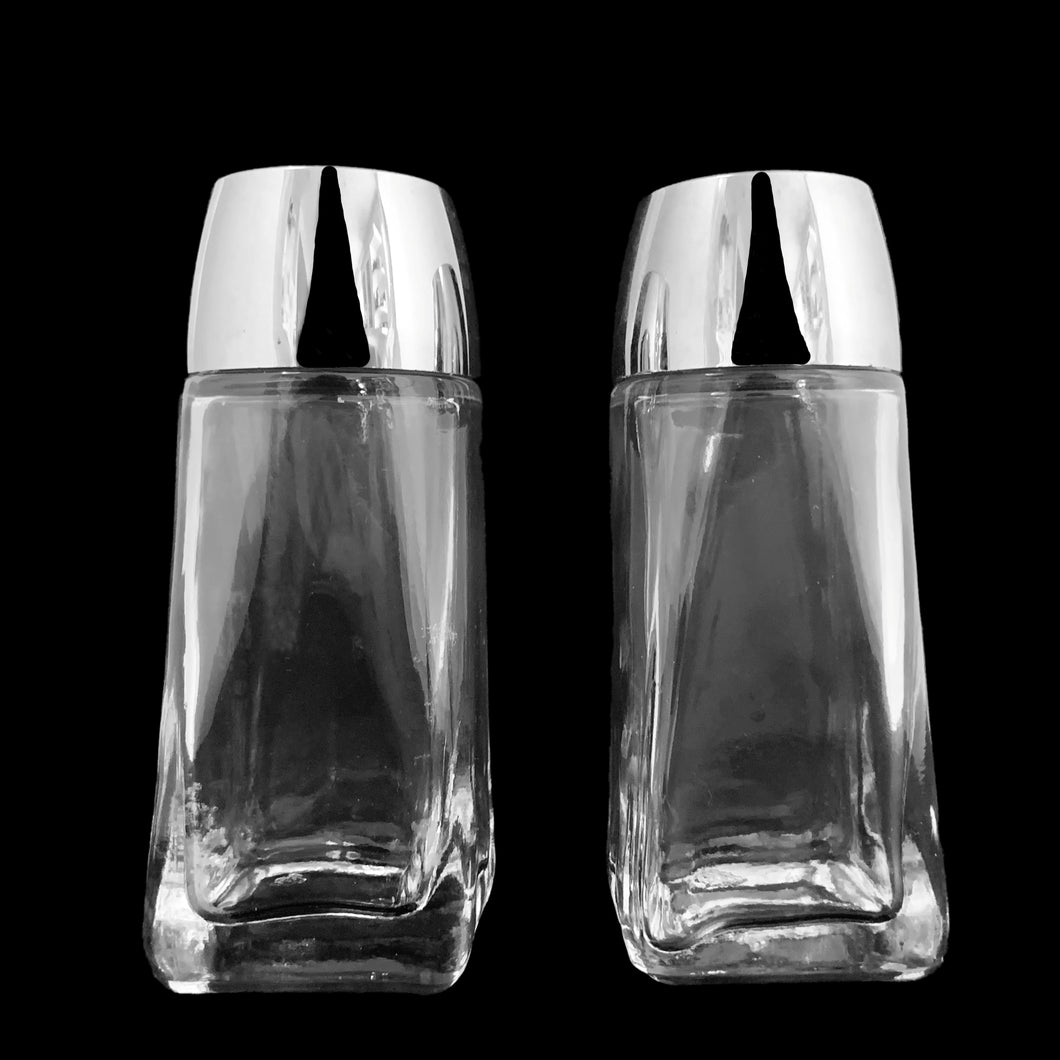 Sail away to flavor-town with this retro vintage set of salt and pepper shakers! These retro-style clear pressed glass shakers feature smooth sides and plasticized chrome screw-on lids. Crafted by Anchor Hocking, circa 1990s. Season your food with a real blast from the past!   The glass is in excellent condition, free from chips/cracks. The lids have very minor wear, see photos. Marked on the bottom.  Measures 1 5/8 x 4 1/8 inches