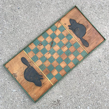 Load image into Gallery viewer, This vintage handmade primitive pine wood checker chess board features a natural, green and black stain, adorned with hand carved beavers at either end. It&#39;s a great addition to family game nights at the cottage, or as a rustic wall hanging to add a touch of nature-inspired charm to your decor.

In good vintage condition. Wired on the back for wall hanging.

Measures 12 1/2 x 24 3/4 x 1 1/4 inches
