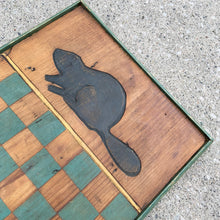 Load image into Gallery viewer, This vintage handmade primitive pine wood checker chess board features a natural, green and black stain, adorned with hand carved beavers at either end. It&#39;s a great addition to family game nights at the cottage, or as a rustic wall hanging to add a touch of nature-inspired charm to your decor.

In good vintage condition. Wired on the back for wall hanging.

Measures 12 1/2 x 24 3/4 x 1 1/4 inches
