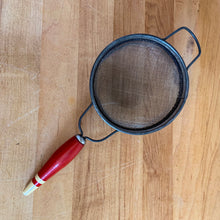 Load image into Gallery viewer, Depression era vintage handheld metal kitchen sieve with a red and cream painted wood handle and hanging loop. Add some charm to your farmhouse or cottage with this useful gadget!

In vintage condition.

Measures 4 1/8 x 9 3/4 x 2 inches
