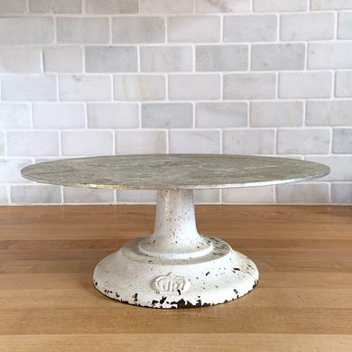 Vintage revolving cake decorating stand featuring a solid cast iron base and aluminum turntable. The base is painted off white and embossed with the initials JR inside a crown. Perfect to use as intended, or to display cakes, baked good or use to create a special display of your favourite vintage treasures. A wonderful accessory for a vintage kitchen with a vintage or farmhouse theme or old fashioned bakery.  In used vintage condition with nice chippy paint.  11 3/4 x 4 1/2 inches   