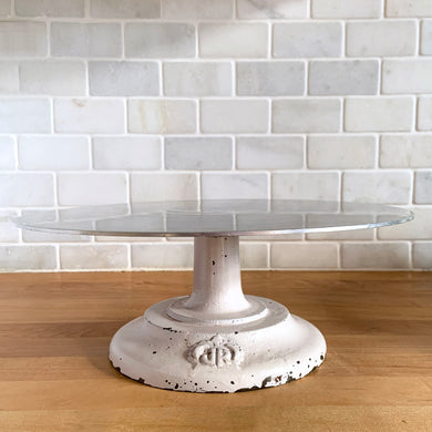 Vintage revolving cake decorating stand featuring a solid cast iron base and aluminum turntable. The base is painted in a putty colour and embossed with the initials JR inside a crown. Perfect to use as intended, or to display cakes, baked good or use to create a special display of your favourite vintage treasures. A wonderful accessory for a vintage kitchen with a vintage or farmhouse theme or old fashioned bakery.  In used vintage condition with nice chippy paint.  11 3/4 x 4 1/2 inches   