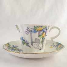 Load image into Gallery viewer, Vintage art deco white bone china teacup and saucer is absolutely gorgeous! Produced by Royal Albert, England, circa 1927 - 1935. Decorated in the &quot;Rosalie&quot; pattern which depicts a hand painted garden path featuring a trellis filled with blue, purple and yellow flowers, trimmed with gold gilt. Excellent condition, free from chips, cracks and repairs. Maker&#39;s marks are on the bottom. Teacup measures 3 3/8 x 2 3/4 inches | Saucer measures 5 1/4 inches
