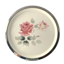 Load image into Gallery viewer, Vintage round metal serving tray featuring an enamled design of pink roses on a cream ground, with polished rim. Crafted by Cassidy's Ltd. Canada, 1960s. A gorgeous way to serve your guests or use as decor.

In excellent condition. Original sticker.

Measures 12 1/2 inch diameter
