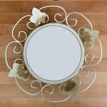 Load image into Gallery viewer, Bring on the retro vintage vibes with this round convex mirror encased in cream painted wrought iron scrolled frame and metal flowers with a touch of gold. The mirror has a metal backing and a built in wall hanger.&nbsp;Circa 1970s. This beauty is ready to hang and is sure to add a special touch of glam to your bath, bedroom or entranceway!

In excellent condition. Marked Made in England.

Measures 12 1/4 inches in diameter

