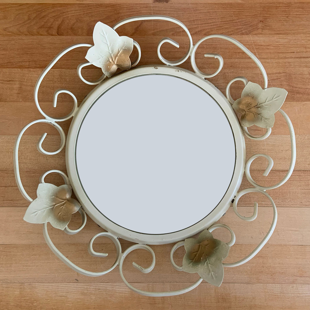 Bring on the retro vintage vibes with this round convex mirror encased in cream painted wrought iron scrolled frame and metal flowers with a touch of gold. The mirror has a metal backing and a built in wall hanger. Circa 1970s. This beauty is ready to hang and is sure to add a special touch of glam to your bath, bedroom or entranceway!

In excellent condition. Marked Made in England.

Measures 12 1/4 inches in diameter