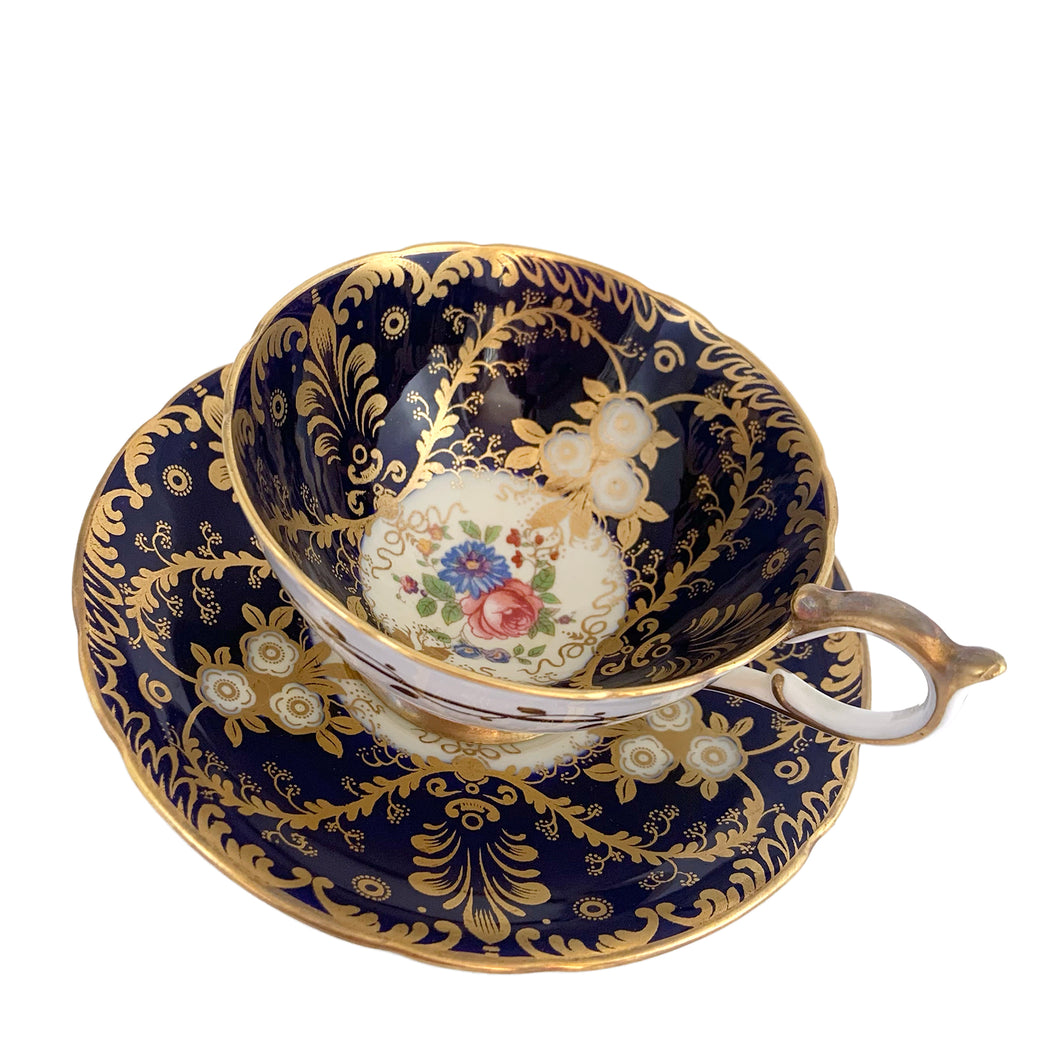 Vintage Royalty Bone China teacup and saucer features a hand painted cobalt blue interior on a white ground, lavishly decorated with gold gilt flowers and fluorishes, complemented by colourful florals in the bottom of the cup and centre of the saucer. Aynsley, England. 1934 - 1950s.  In excellent condition, no chips/cracks/repairs.  Teacup measures 4 x 2 1/4 Saucer measures 5 3/4