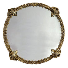 Load image into Gallery viewer, Stunning example of a vintage Hollywood Regency style round mirrored vanity tray featuring a border of brass filigree flower blossoms with a seated cherub on each of the four feet to guard your treasures. Adds a touch of glamour to bath or bedroom decor!  In excellent used vintage condition.  Measures 8 3/4 inches from foot to foot

