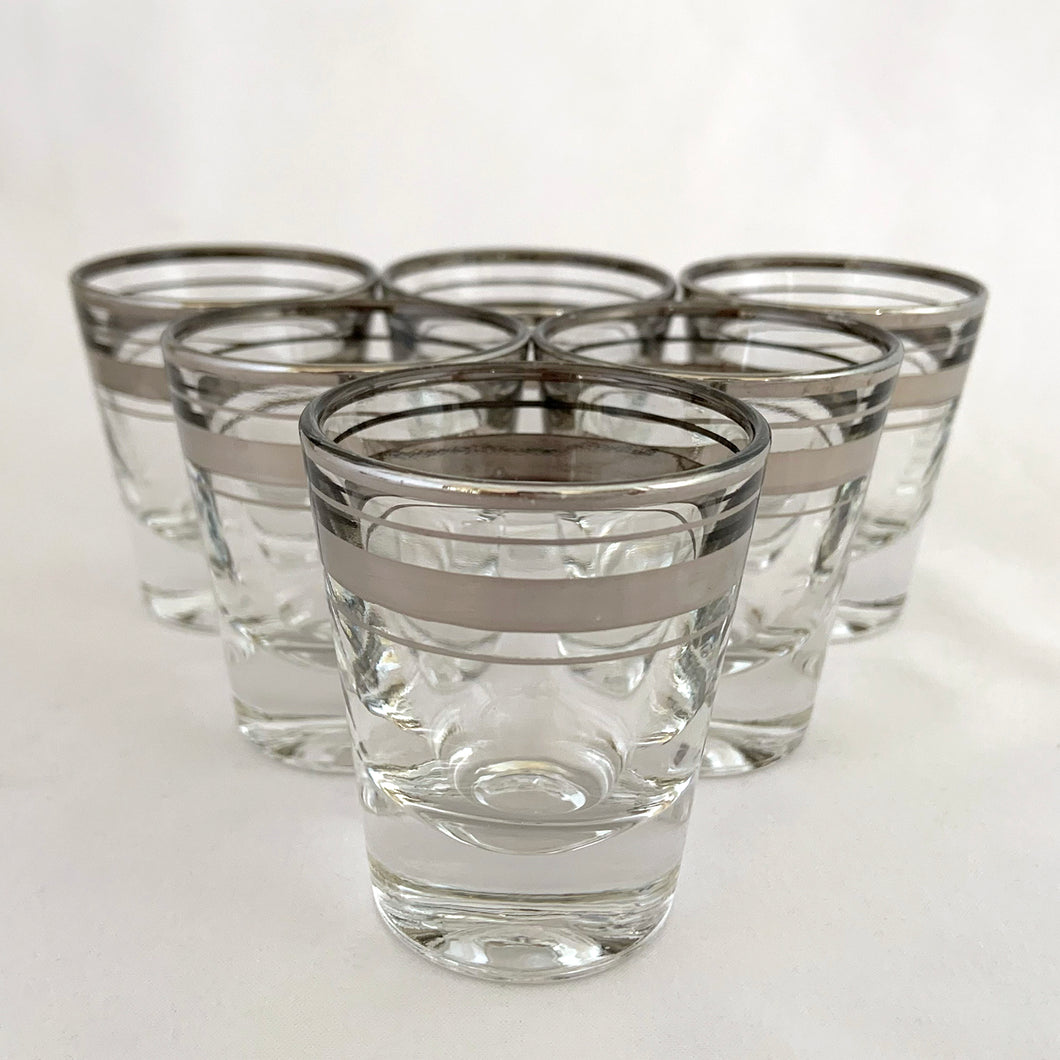 Set of six vintage mid-century era silver banded and rimmed shot glasses. Libbey Glass, USA, 1960s. Add some Hollywood Regency glam to your barware collection with these beauties!

Good vintage condition, no chips, minor wear to the silver.

Measures 1 7/8 x 2 1/4 inches

Capacity 1 ounce