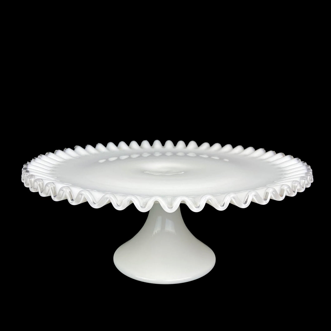 This vintage milk glass Silver Crest round cake stand features a classic clear crimped edge. Crafted by Fenton Art Glass, USA, between 1942 - 1986. A stunning example of mid-century tableware that will always be in style no matter your decor style! An elegant way to present cakes and desserts whether for everyday entertaining, a wedding or bridal shower!

In excellent condition, no chips. Unmarked.

Measures 13 x 5 inches