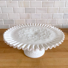 Load image into Gallery viewer, This vintage milk glass &quot;Silver Crest Spanish Lace&quot; round cake stand features a classic clear crimped edge and a raised hearts and swirls design. Crafted by the Fenton Art Glass, USA, between 1942 - 1969. A stunning example of mid-century tableware that will always be in style no matter your decor style! An elegant way to present cakes and desserts whether for everyday entertaining, a wedding or bridal shower! In excellent condition, free from chips. Unmarked. Measures 11 x 4 1/2 inches
