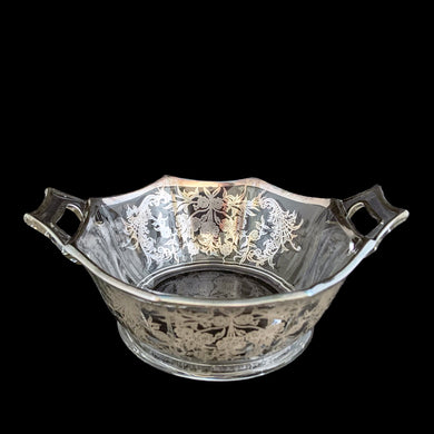 A lovely octagon shaped clear glass handled bowl featuring an art deco style decorative silver overlay of floral swags. The perfect size for candies or nuts and is easily repurposed as a trinket dish.   In excellent condition, free from chips/cracks and the silver overlay is intact.  Measures 6 5/8 x 3 1/8 inches (incl. handles)