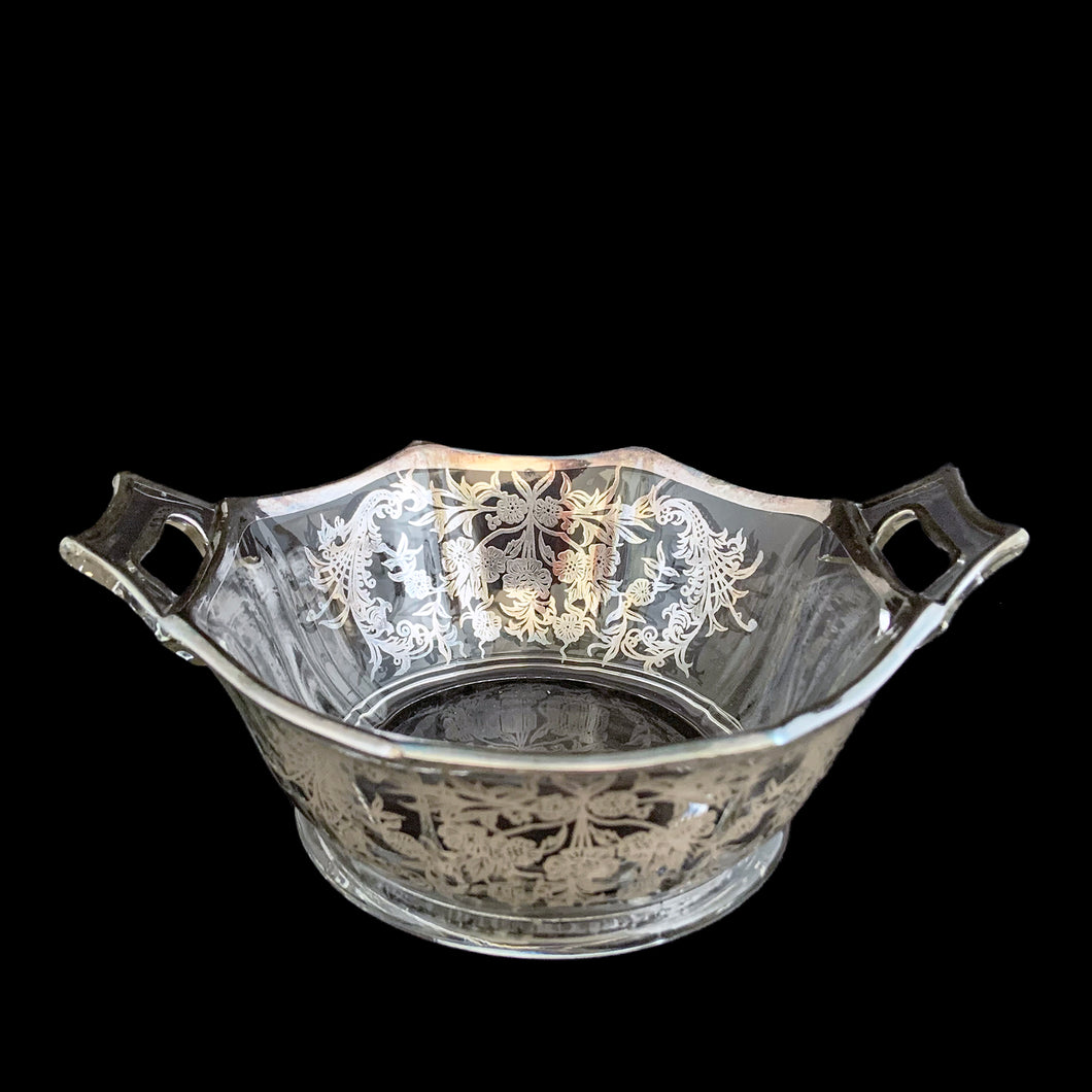 A lovely octagon shaped clear glass handled bowl featuring an art deco style decorative silver overlay of floral swags. The perfect size for candies or nuts and is easily repurposed as a trinket dish.   In excellent condition, free from chips/cracks and the silver overlay is intact.  Measures 6 5/8 x 3 1/8 inches (incl. handles)