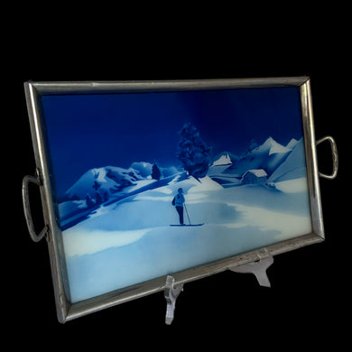 Stunning vintage art deco style reverse painted tray with metal frame and handles features a winter landscape, skier with pipe in shades of blue and white. Crafted in Germany, 1920s. Perfect as a vanity tray, to serves drinks and snacks or even wall art.

The painting is in excellent condition with age-related wear to the frame.

Measures 15 1/2 x 10 (not incl. handles)