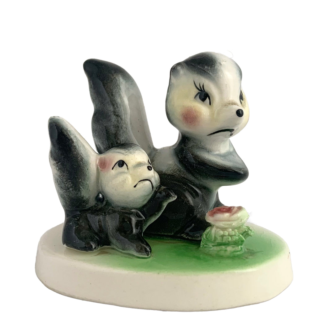 Vintage mid-century kitsch ceramic figures of a skunk mama and baby with a sweet pink flower on a stand. Crafted in Japan, circa 1950s. An adorable figurine to add to your mid-century animal figurine collection.  In excellent condition, no chips/cracks/repairs.  Measures 3 1/2 x 2 5/8 x 3 inches