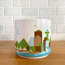 Load image into Gallery viewer, Perfect for your morning cuppa joe to make you feel like a world traveller! This fabulous collectible VANCOUVER ceramic mug was produced by Starbucks as part of their YOU ARE HERE collection, 2014. A white ceramic mug printed design in shades of green blue, brown and red with blue interior. Celebrate the By Sea, Land, and Air We Prosper city!

In excellent condition, free from chips/cracks/wear.

Measures 3 5/8 x 3 3/8 inches

Capacity 14 ounces
