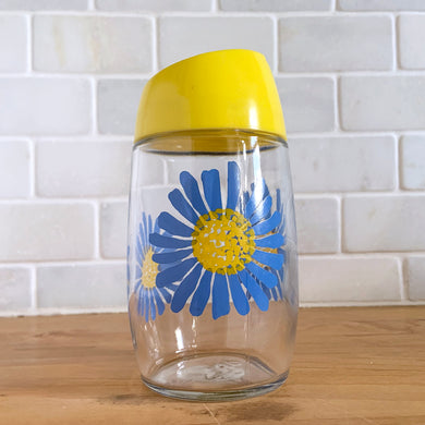 Classic vintage clear glass sugar dispenser, decorated with a series of blue flowers with yellows centres, topped with a bright yellow flip top plastic lid. Crafted by Dominion Glass Canada, circa 1980s.  Glass is in excellent condition, free from chips/cracks.  Measures 2 3/4 x 5 1/2 inches