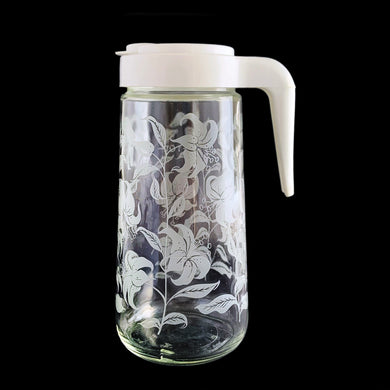 Vintage Tang promotional clear glass pitcher decorated with white enamel lilies and topped off with an open handled plastic lid with 