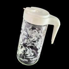 Load image into Gallery viewer, Vintage Tang promotional clear glass pitcher decorated with white enamel lilies and topped off with an open handled plastic lid with &quot;Tang&quot; impressed on the top. Crafted by Anchor Hocking, USA, circa 1970s. A great pitcher for your favourite beverage!  In excellent condition.  Measures 4 x 8 3/4 inches
