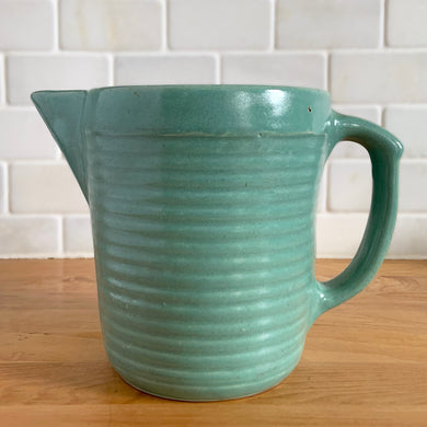 Vintage teal glazed horizontal ribbed stoneware pitcher. Crafted by Monmouth Western Stoneware, USA, 1920s. Add this solid utilitarian piece to your farmhouse decor or art pottery collection!

In excellent condition, no chips/cracks/repairs, age-related crazing. Maker's mark.

Measures 7 3/8 x 4 1/2 x 5 inches (incl. spout and handle)