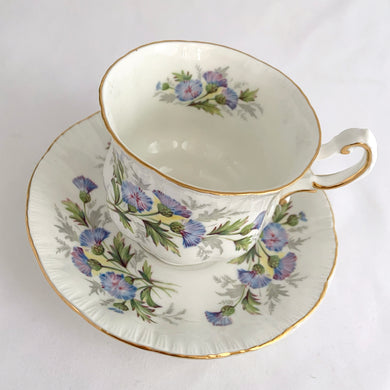 Stunning vintage white porcelain teacup and matching saucer decorated featuring thistle flowers in shades of purple and green plus gold gilt details with a spray of flowers on the interior of the teacup. Part of the English Flowers series produced by The Paragon China Company, England, circa 1950.  In excellent condition, free from chips/cracks/repairs. Marked on the bottom with single warrant stamp.  Teacup measures 3 1/8 x 2 3/4 inches  Saucer measures 5 3/8 inches
