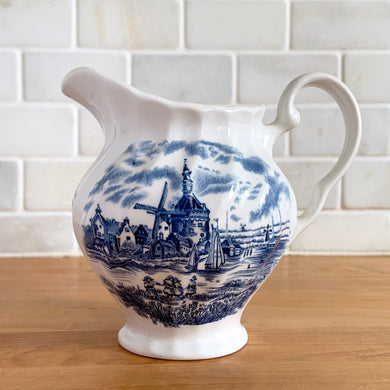 Vintage Tulip Time blue transferware ceramic creamer on white ground with swirl border features an intricate scene depicting a Dutch village, complete with windmills, cottages, and boats. Crafted by Johnson Brothers, England, 1962 - 1977. A lovely addition to your tablescape!

In excellent condition, no chips.

Measures 4 3/8 inches

Capacity 10 ounces