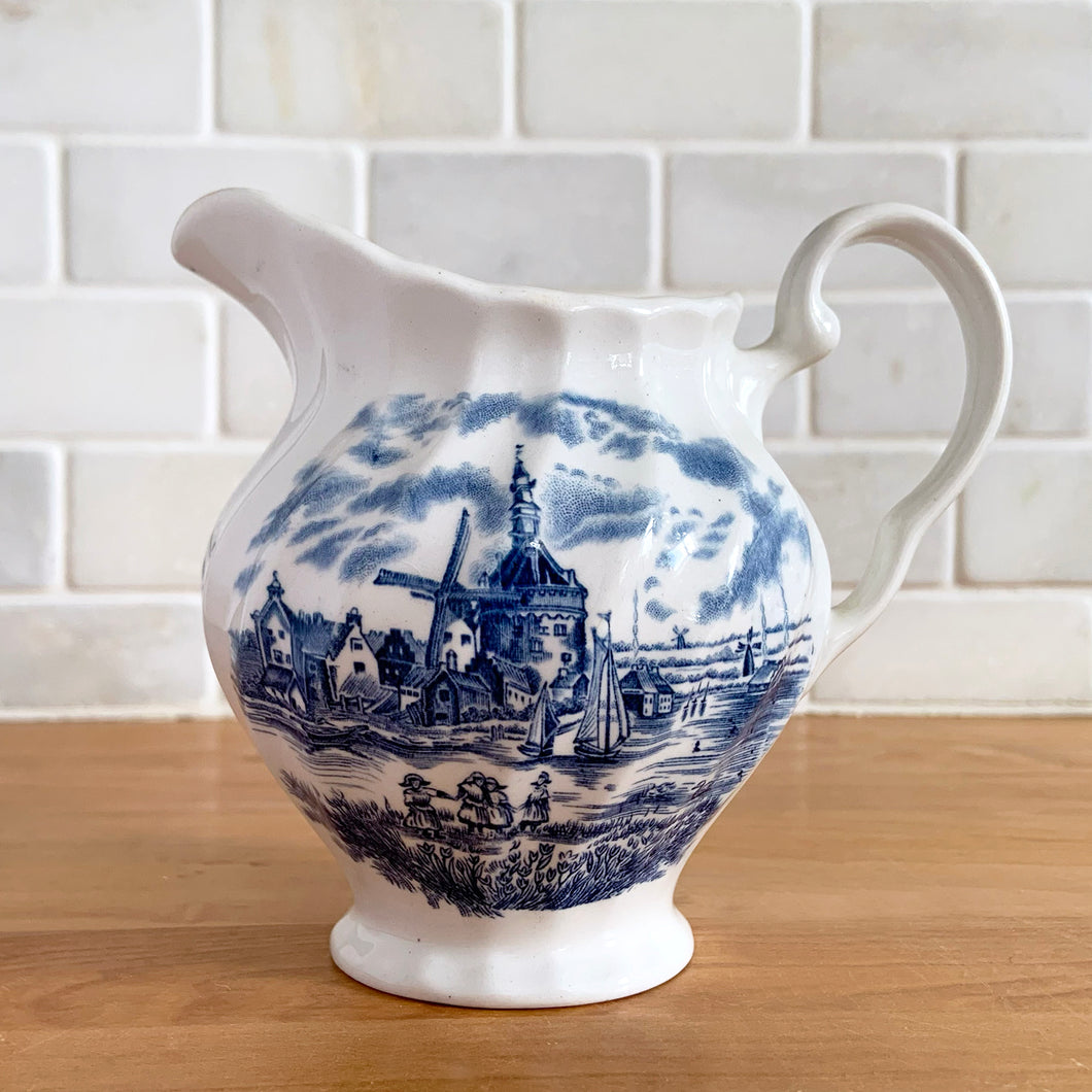 Vintage Tulip Time blue transferware ceramic creamer on white ground with swirl border features an intricate scene depicting a Dutch village, complete with windmills, cottages, and boats. Crafted by Johnson Brothers, England, 1962 - 1977. A lovely addition to your tablescape!

In excellent condition, no chips.

Measures 4 3/8 inches

Capacity 10 ounces