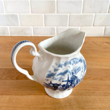 Load image into Gallery viewer, Vintage Tulip Time blue transferware ceramic creamer on white ground with swirl border features an intricate scene depicting a Dutch village, complete with windmills, cottages, and boats. Crafted by Johnson Brothers, England, 1962 - 1977. A lovely addition to your tablescape!

In excellent condition, no chips.

Measures 4 3/8 inches

Capacity 10 ounces
