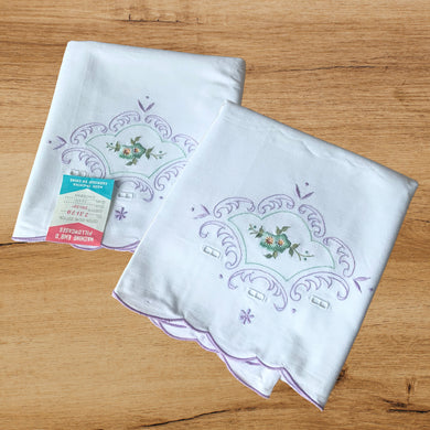A lovely pair of vintage white cotton pillowcases, featuring elegantly design of hand embroidered turquoise flowers with green leaves, surrounded by cutwork and a border of lilac purple and aqua flourishes and flowers, plus a finished scalloped edge. A gorgeous addition to your bed linens!  In excellent condition. New old stock with original tags.  Measures 31 1/2 x 19 1/2 inches   