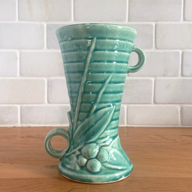 Vintage Art Deco gloss turquoise ring handled trumpet vase with leaves and berries on a ringed body. Crafted by McCoy Pottery, 1940s. This rare piece is must for any McCoy art pottery collector!

In as found vintage condition, no chips/repairs, tight hairline crack and crazing commensurate with age. Unmarked.

Measures 3 1/4 x 5 3/4 inches