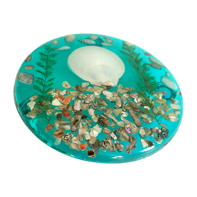 Sparkling abalone and sea shells adorn this stunning vintage turquoise Lucite round trivet. Crafted by Unique Designs, USA, circa 1970s. Add some glam seaside style to your table with this striking trivet!  In excellent vintage condition, minor wear. Original label.  Measures 6 1/2 inches