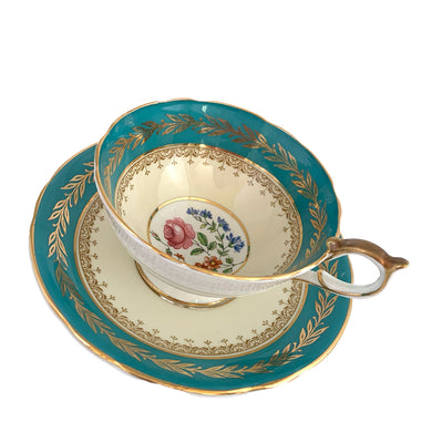 This highly sought after vintage Bone China teacup and saucer with scalloped rim features a hand painted turquoise and pale yellow banded interior on a white ground, lavishly decorated with gold gilt filigree, complemented by colourful floral bouquets in the bottom of the cup and centre of the saucer. Crafted by Aynsley, England. Backstamp indicates production between 1934 - 1950s. A stunning addition to your teacup collection!