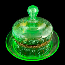 Load image into Gallery viewer, Antique Victorian era hand blown green uranium glass covered butter dish featuring gold, white and blue enamel decoration. Glows beautifully under black light. Crafted by Fenton Art Glass, USA, early 20th century. A stunning piece to add to your glass collection.

In as found vintage condition with wear to the enamel and chips to the dish rim and roughess to the lid rim.

Measures 7 1/8 x 7 1/8 x 5 1/2 inches
