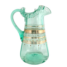 Load image into Gallery viewer, Antique Victorian era green uranium glass pitcher featuring gold, white and red enamel decoration with ruffle crimped rim and an applied handle. Glows beautifully under black light. Crafted by Fenton Art Glass, USA, early 20th century. A stunning piece to add to your glass collection.

In as found vintage condition with wear to the enamel. There is a stringer in the handle and a chip to the base of the handle itself.

Measures 5 3/4 x 8 x 10 inches
