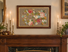 Load image into Gallery viewer, In situ AI mock up of an Antique Victorian floral needlepoint under glass in a dark wooden frame with gold inner trim, featuring pink and red roses, hanging over a wood fireplace flanked by brass candlesticks
