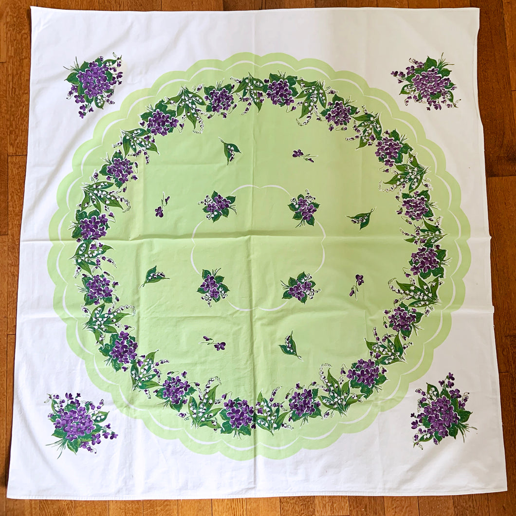 This vintage cotton tablecloth features a central scalloped apple green medallion bordered in white with beautiful purple violets on a white and green background. An elegant and traditional accent for any décor, made from high quality cotton.  In excellent condition.  Measures 50 x 47 1/2 inches
