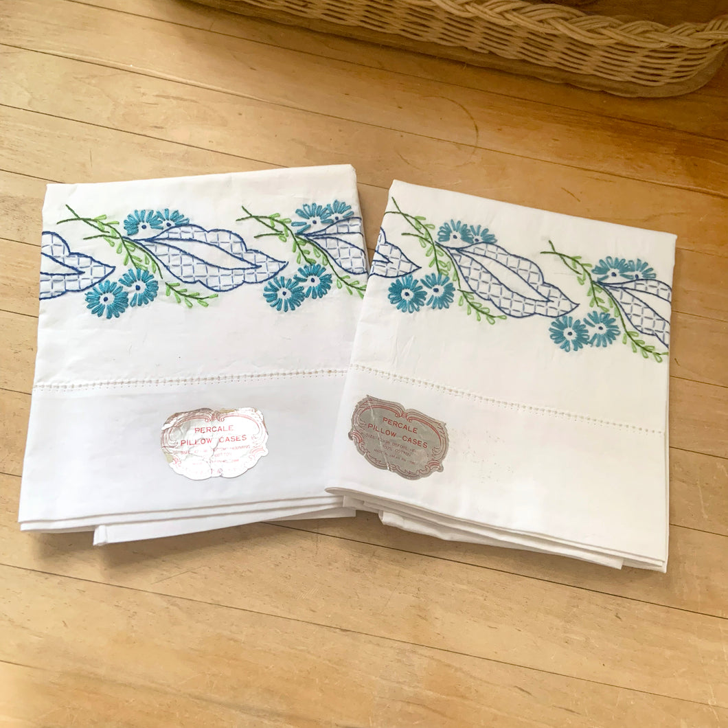 A lovely pair of vintage white 100% percale cotton pillowcases, hand embroidered with a blue daisy flowers, graphic blue leaves. These new old stock linens will be a gorgeous addition to your bedding!

In excellent condition, free from tears. Age-related yellowing at the bands. Original stickers, made in Japan.

Measures 30 3/4 x 18 inches