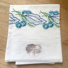 Load image into Gallery viewer, A lovely pair of vintage white 100% percale cotton pillowcases, hand embroidered with a blue daisy flowers, graphic blue leaves. These new old stock linens will be a gorgeous addition to your bedding!

In excellent condition, free from tears. Age-related yellowing at the bands. Original stickers, made in Japan.

Measures 30 3/4 x 18 inches

