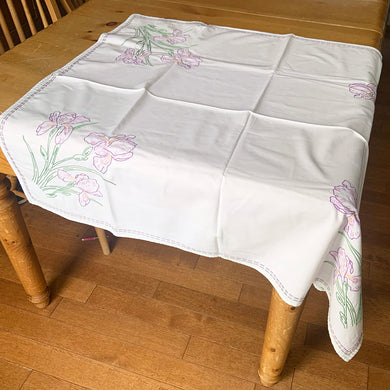 Pretty vintage white cotton tablecloth featuring hand embroidered Iris flowers in each corner in shades of purple, pink, yellow and green. Finished with a dashed border of purple, pink and green. In excellent condition, free from stains/tears. Measures 33 1/2 x 38 inches