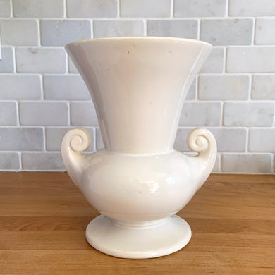Vintage mid-century gloss white trumpet vase with curled handles. Crafted by McCoy Pottery, late 1950s. This lovely vase is must for any art pottery collector!

In as found vintage condition, chip to the exterior rim, no cracks/repairs, crazing commensurate with age. Maker's mark on the bottom.

Measures 6 1/4 x 5 7/8 x 8 inches
