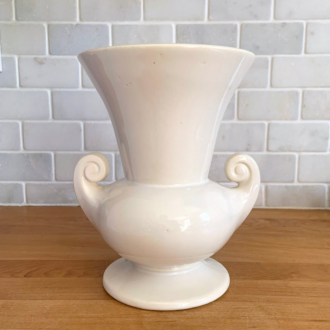 Vintage mid-century gloss white trumpet vase with curled handles. Crafted by McCoy Pottery, late 1950s. This lovely vase is must for any art pottery collector!

In as found vintage condition, chip to the exterior rim, no cracks/repairs, crazing commensurate with age. Maker's mark on the bottom.

Measures 6 1/4 x 5 7/8 x 8 inches