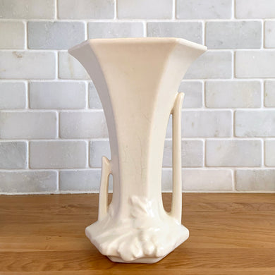 Vintage Art Deco matte white trumpet vase features a unique stretch hexagonal shape and asymmetric handles with leaf and berry motif. Crafted by Nelson McCoy Pottery, 1940s. This rare piece is must for any art pottery collector! A lovely way to enhance your home's decor or give as a gift!

In excellent vintage condition, no chips/cracks/repairs. Typical age-related crazing, manufacturer's glaze pops. Maker's mark.

Measures 5 1/2 x 4 1/4 x 8 inches