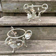 Load image into Gallery viewer, Pair of white vintage mid-century era shabby chic wrought iron metal garden plant stands decorated with grapevines. Includes pink plastic pot inserts. Perfect for your favourite plants.

In as found vintage condition.

Plant stands measure 6 1/2 x 5 1/2 inches

Plastic pots measure 4 3/8 x 3 3/4 inches
