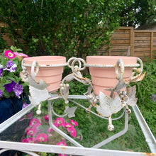 Load image into Gallery viewer, Pair of white vintage mid-century era shabby chic wrought iron metal garden plant stands decorated with grapevines. Includes pink plastic pot inserts. Perfect for your favourite plants.&nbsp;

In as found vintage condition.

Plant stands measure 6 1/2 x 5 1/2 inches

Plastic pots measure 4 3/8 x 3 3/4 inches
