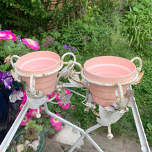Load image into Gallery viewer, Pair of white vintage mid-century era shabby chic wrought iron metal garden plant stands decorated with grapevines. Includes pink plastic pot inserts. Perfect for your favourite plants.&nbsp;

In as found vintage condition.

Plant stands measure 6 1/2 x 5 1/2 inches

Plastic pots measure 4 3/8 x 3 3/4 inches
