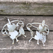 Load image into Gallery viewer, Pair of white vintage mid-century era shabby chic wrought iron metal garden plant stands decorated with grapevines. Includes pink plastic pot inserts. Perfect for your favourite plants.

In as found vintage condition.

Plant stands measure 6 1/2 x 5 1/2 inches

Plastic pots measure 4 3/8 x 3 3/4 inches
