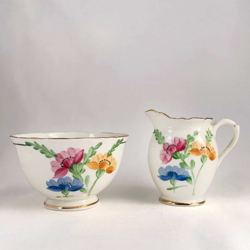 Vintage bone china wild flowers creamer and sugar, featuring hand painted florals in shades of pink, blue, yellow and green with gold gilt trim and scalloped edges. Crafted by Delphine China, England, 1920s. A lovely way to enhance your tea and coffee experience!

In excellent condition, no chips, cracks or repairs. Maker's mark on the bottom.

Creamer measures 1 7/8 x 2 3/4 inches | Sugar measures 3 5/8 x 2 1/4 inches