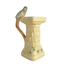 Load image into Gallery viewer, Beautifully detailed, vintage Art Deco Flaxman Ware matte yellow glazed castle tower pitcher featuring a budgie bird atop the handle, along with purple and green florals. Crafted by Wade, Heath &amp; Co., England, 1930s. This decorative and highly collectible piece makes a lovely decor accent.

In good vintage condition with chip on the bottom of the foot, typical crazing. Maker&#39;s mark on the bottom.

Measures 5 x 4 x 7 3/4 inches
